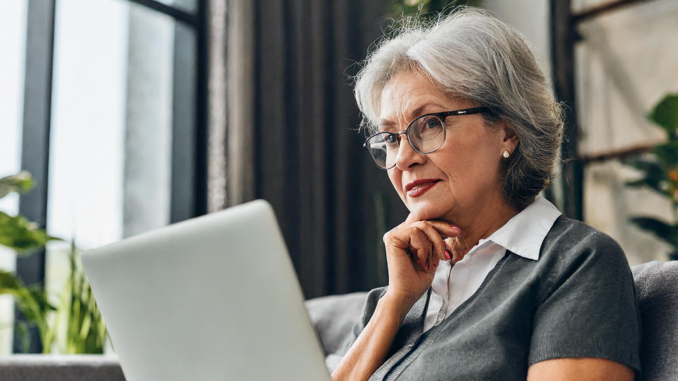 Síndica de condomínio, no sofá de casa, olhando notebook com semblante preocupado